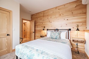 A bedroom with a wooden headboard, a bed with floral bedding, bedside lamps, and a nightstand. - Heated Pool in Winter, Sleeps 18, 10 Min to Sunday River, Mountain Views (Bethel)