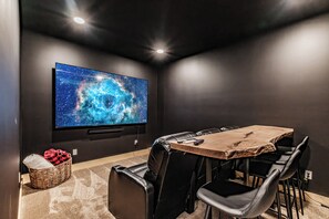A home theater room with a large flat-screen TV, leather seating, and a wooden table. - Heated Pool in Winter, Sleeps 18, 10 Min to Sunday River, Mountain Views (Bethel)