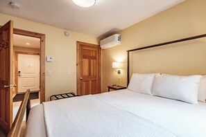 A hotel room with a bed, a bedside table, a lamp, and a door.