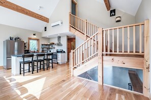 A modern kitchen with a central island, wooden flooring, and a staircase with glass railings.