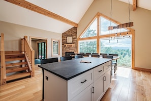 A modern kitchen with a large island, wooden staircase, and a stone fireplace. - Heated Pool in Winter, Sleeps 18, 10 Min to Sunday River, Mountain Views (Bethel)