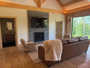 Un salón con chimenea, vigas de madera, un sofá y vistas a árboles.