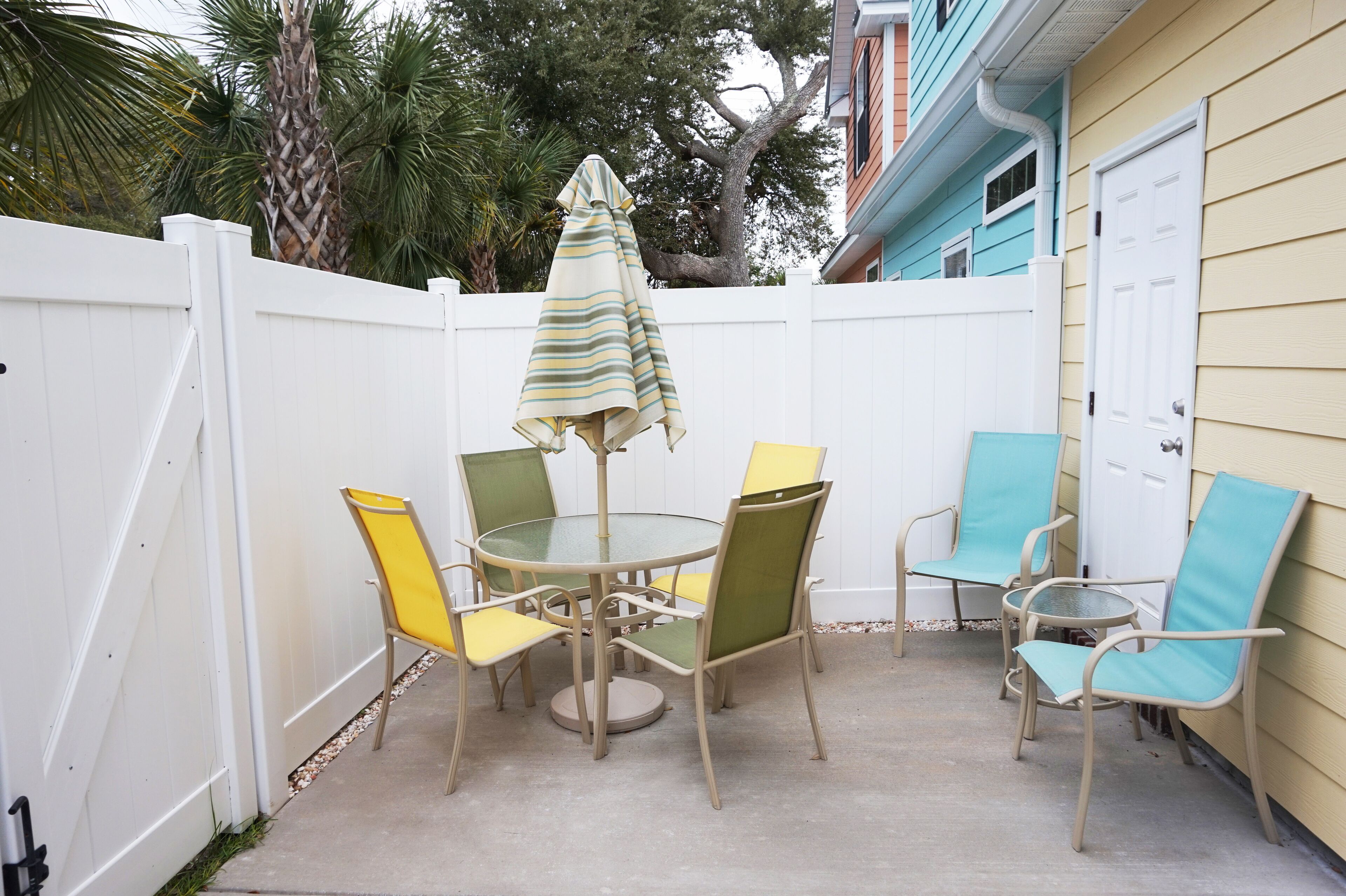 A patio with a round table and chairs, an umbrella, and a white fence.