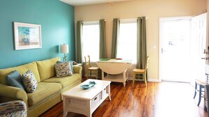 A living room with a yellow couch, a white coffee table, a ceiling fan, and a dining table with chairs. - Beautiful Beach Style Cottage, One Block from Beach.  (Myrtle Beach)