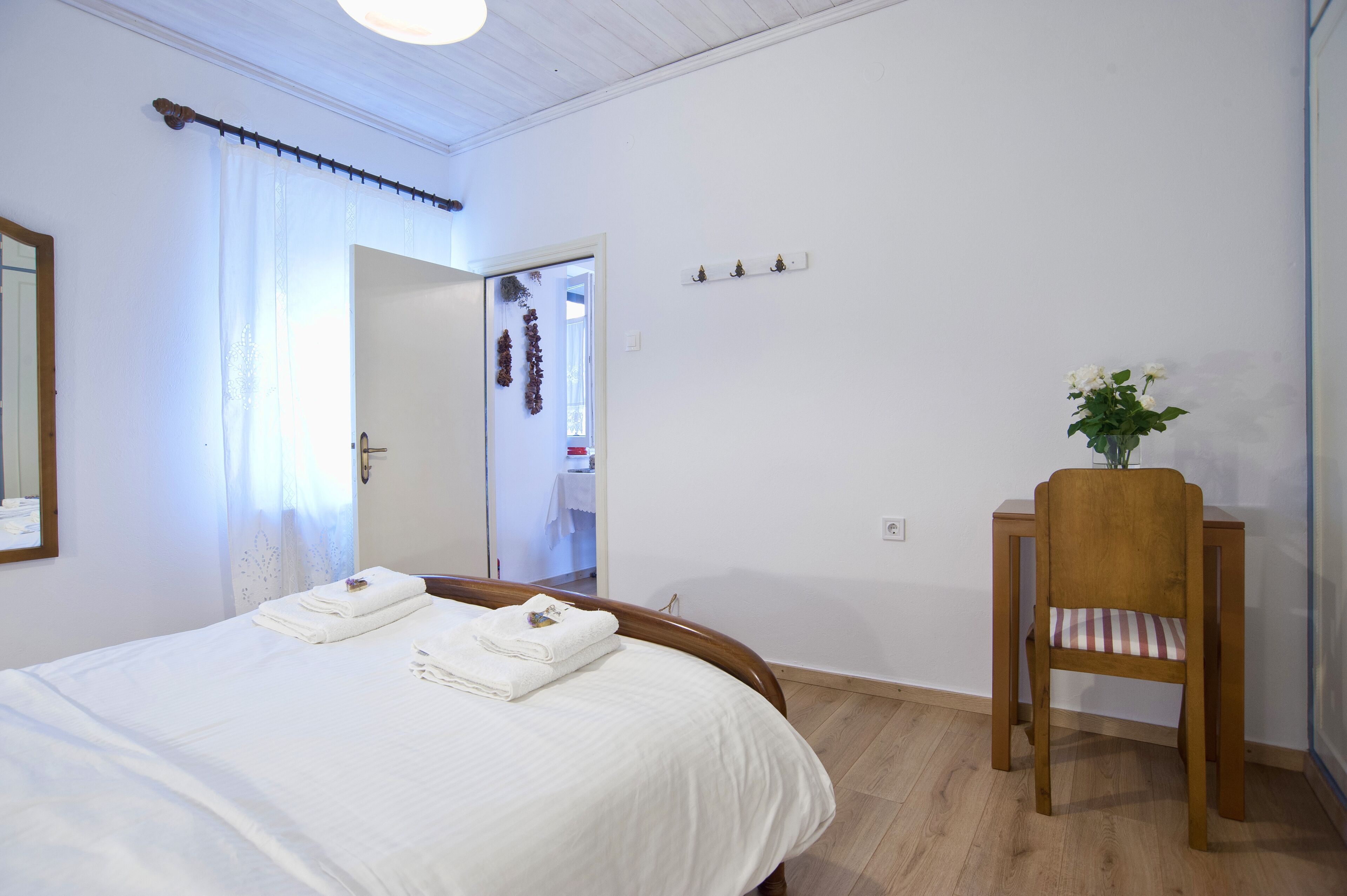 Une chambre d’hôtel avec un lit bien fait, une chaise en bois, une petite table et un miroir au mur.