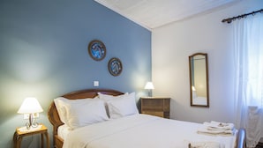 Ein ordentlich bezogenes Bett mit weißen Leinentüchern, ein Holzkopfschild, zwei an der Wand befestigte Bilderrahmen, ein Nachttisch mit einer Lampe und ein Spiegel an der Wand.
