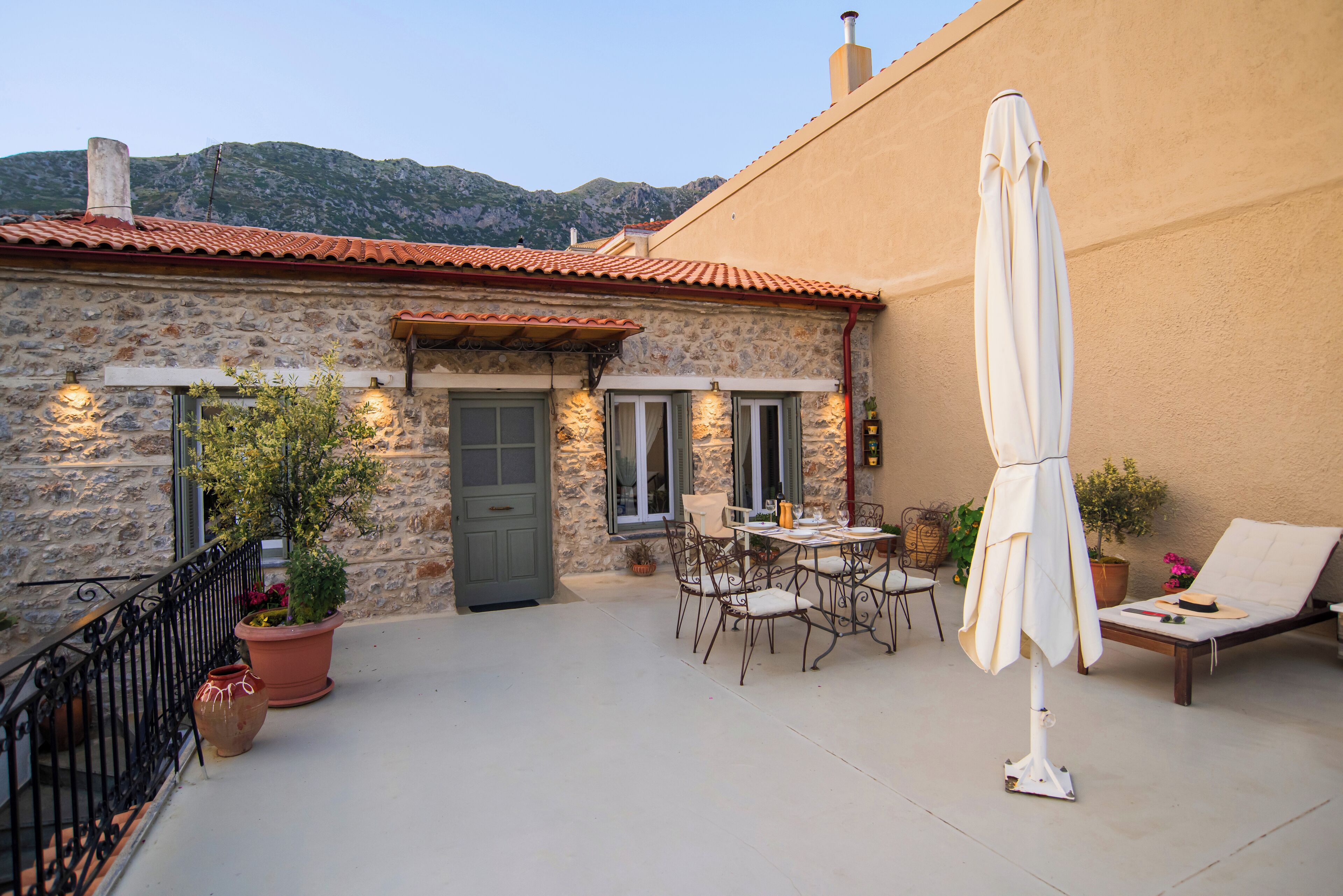 Un bâtiment en pierre avec un toit en tuiles, un balcon avec une table et des chaises, et un parasol blanc.