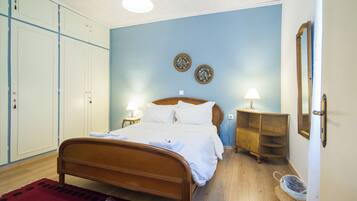 A bedroom with a wooden bed, a red rug, a wooden nightstand, a lamp, and a mirror on the wall.