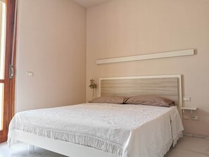 A bedroom with a bed, a bedside table, a wall-mounted shelf, and a door.