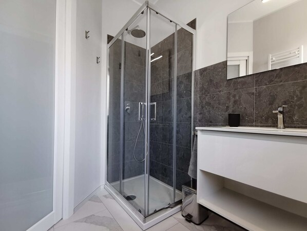 A modern bathroom with a glass-enclosed shower, a white vanity, and dark marble tiles.