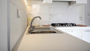 A modern kitchen with a stainless steel sink, a gas stove, and white cabinetry.