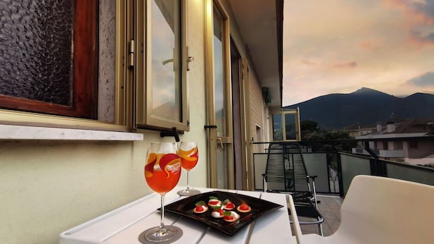 A balcony with a table set for two, featuring a tray of appetizers and two glasses of a red beverage.