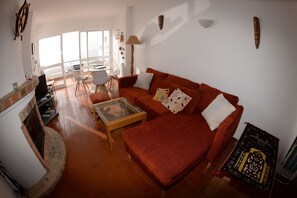 A living room with a red sofa, a glass coffee table, and a fireplace. There is a balcony with a glass door and a chair. - Casa Cian Luxury 8th floor apartment with stunning 270° Sea View,140m from beach (Praia da Luz)