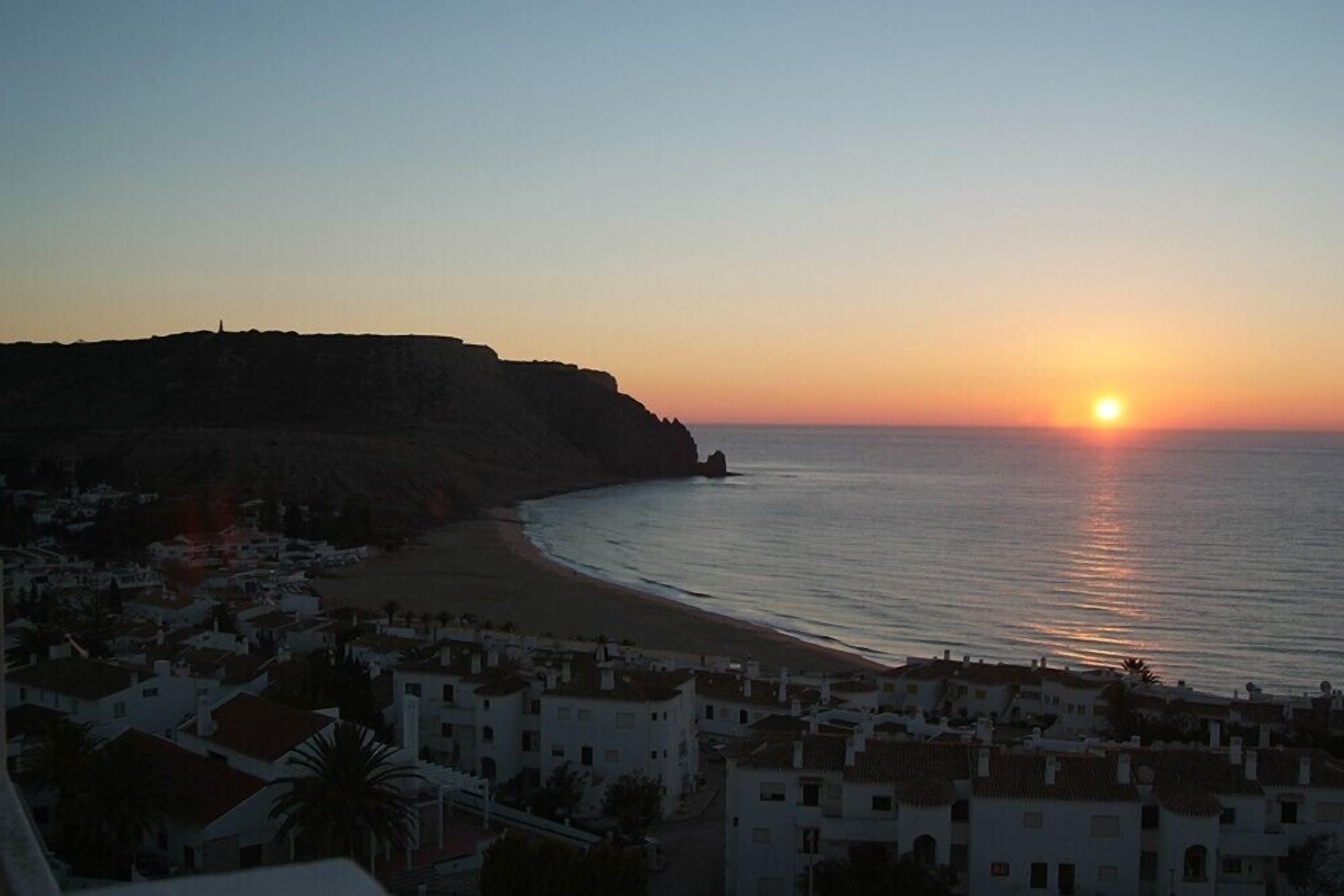 A coastal town at sunset with a beach and buildings in the foreground.