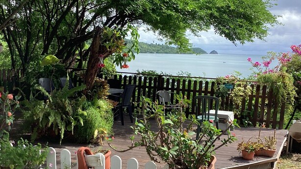 A wooden deck with potted plants and a table with chairs, overlooking a body of water and distant land. - Villa with panoramic view on the islets of Robert and natural swimming pool  (LE ROBERT)