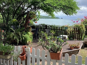 A wooden deck with potted plants and a table with chairs, overlooking a body of water and distant land. - Villa with panoramic view on the islets of Robert and natural swimming pool (LE ROBERT)