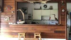 A rustic kitchen with wooden walls, a wooden bench, and various decorative items including a large antler piece above the counter. - Villa with panoramic view on the islets of Robert and natural swimming pool  (LE ROBERT)