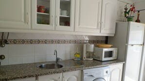 Una cocina con armarios blancos, un lavamanos de acero inoxidable, un microondas, una cafetera y una lavadora.