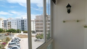 Vista desde una ventana sobre un estacionamiento con varios coches, un edificio de varios pisos y una calle con algo de vegetación.