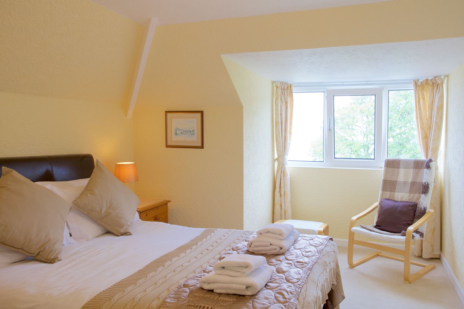 A neatly made bed with pillows, a chair, and a bedside table with a lamp.