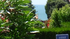 A sign reading "AVENUE des FLOTS" amidst lush greenery and a view of the sea.