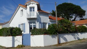 A two-story house with a white facade, a blue door, and a balcony.