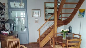 A dining area with a wooden table and chairs, a patterned rug, and a staircase with a wooden railing.