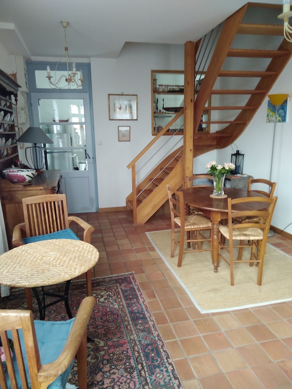 A dining area with a wooden table and chairs, a patterned rug, and a staircase with a wooden railing. - Pornic T2 house aucalme, small sea view, near beach and spa (Pornic)