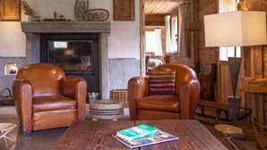 A cozy living room with leather armchairs, a fireplace, and a wooden ceiling.