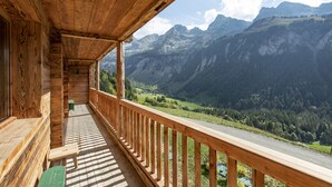 A wooden balcony with a view of a valley and mountains.