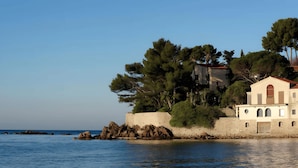 A coastal building with a stone wall, trees, and a view of the sea.