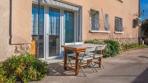 A building with a sliding glass door, a table with chairs, and a small garden area.