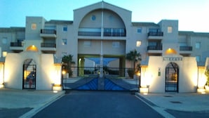 Fachada de hotel con un arco central, varios balcones y letreros iluminados.