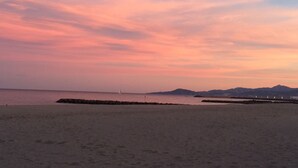 Una playa con un rompeolas rocoso y montañas lejanas bajo un cielo rosa y púrpura.