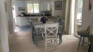 Un vaste espace de vie comprenant un coin repas avec une table et des chaises, une cuisine à l’arrière-plan et une vue à travers une porte vitrée.