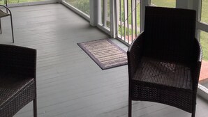 Une véranda abritée, avec un fauteuil en osier et une petite table, donnant sur un lac bordé d’arbres et sur un quai.
