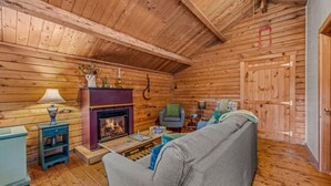 Ein Holzblockhaus-Interieur mit Kamin, einer Couch, einem Tisch mit Spielen und einer Gitarre an der Wand.