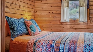Ein Schlafzimmer in einer Holzhütte mit einem Bett, Kissen und einem Fenster mit Vorhängen.