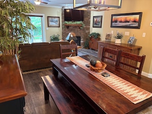 A dining area with a wooden table, benches, and a rug. There is a stone fireplace, a television mounted on the wall, and various framed pictures. - Gatlinburg's Finest Downtown Location, Restaurants, Great Mtn Views, Tranquil (Gatlinburg)