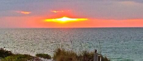 A sunset over a calm sea with a rocky shoreline and a statue.