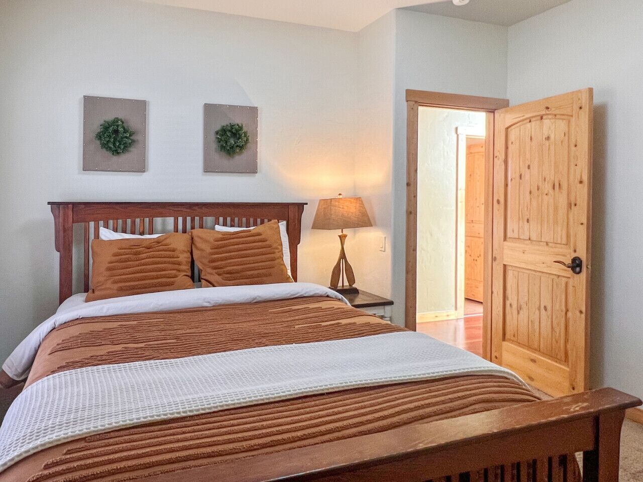 A bedroom with a wooden bed, two wall-mounted lamps, and a wooden door.