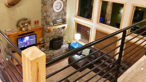 Una sala de estar con chimenea de piedra, cabeza de venado montada, televisor y escalera.
