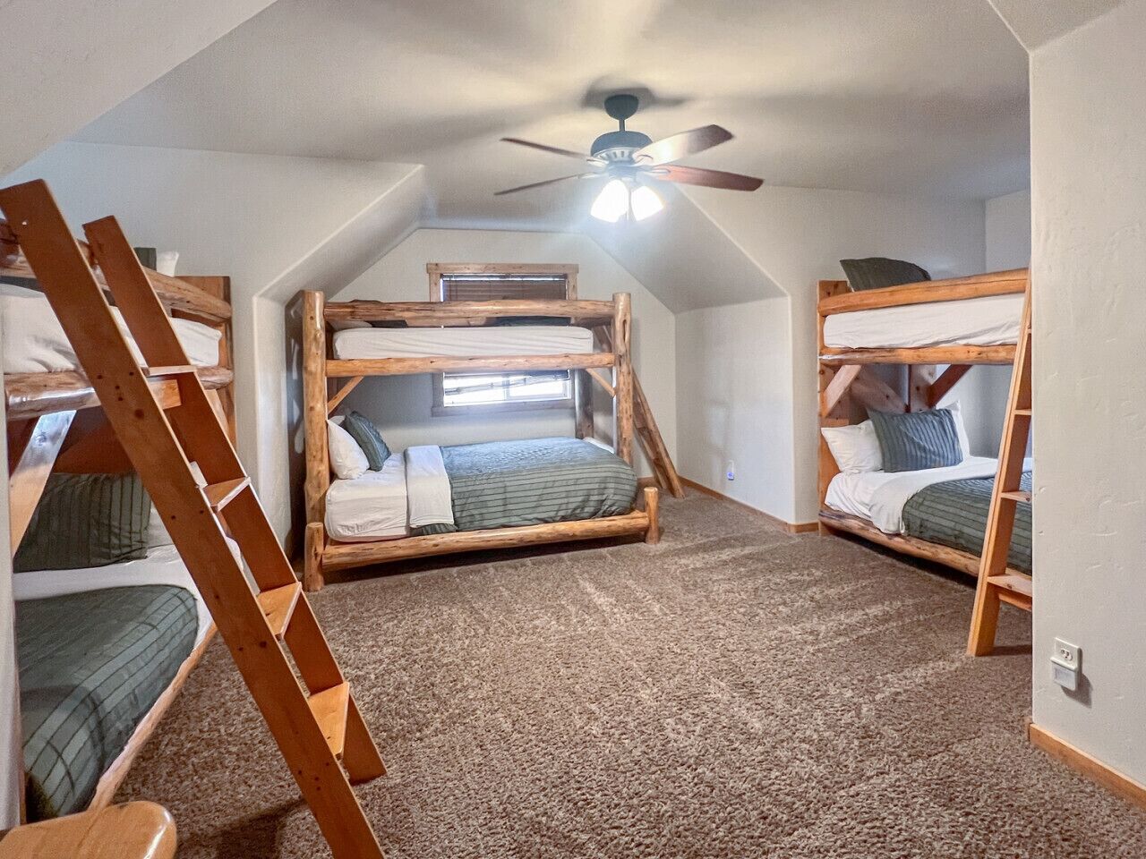 Un dormitorio tipo loft con literas, un ventilador de techo y una ventana.