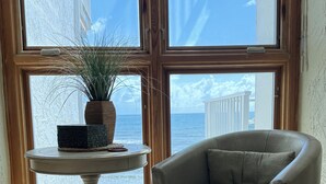 Ein Zimmer mit Meerblick, ein runder Tisch mit einer Pflanze und ein gepolsterter Sessel.