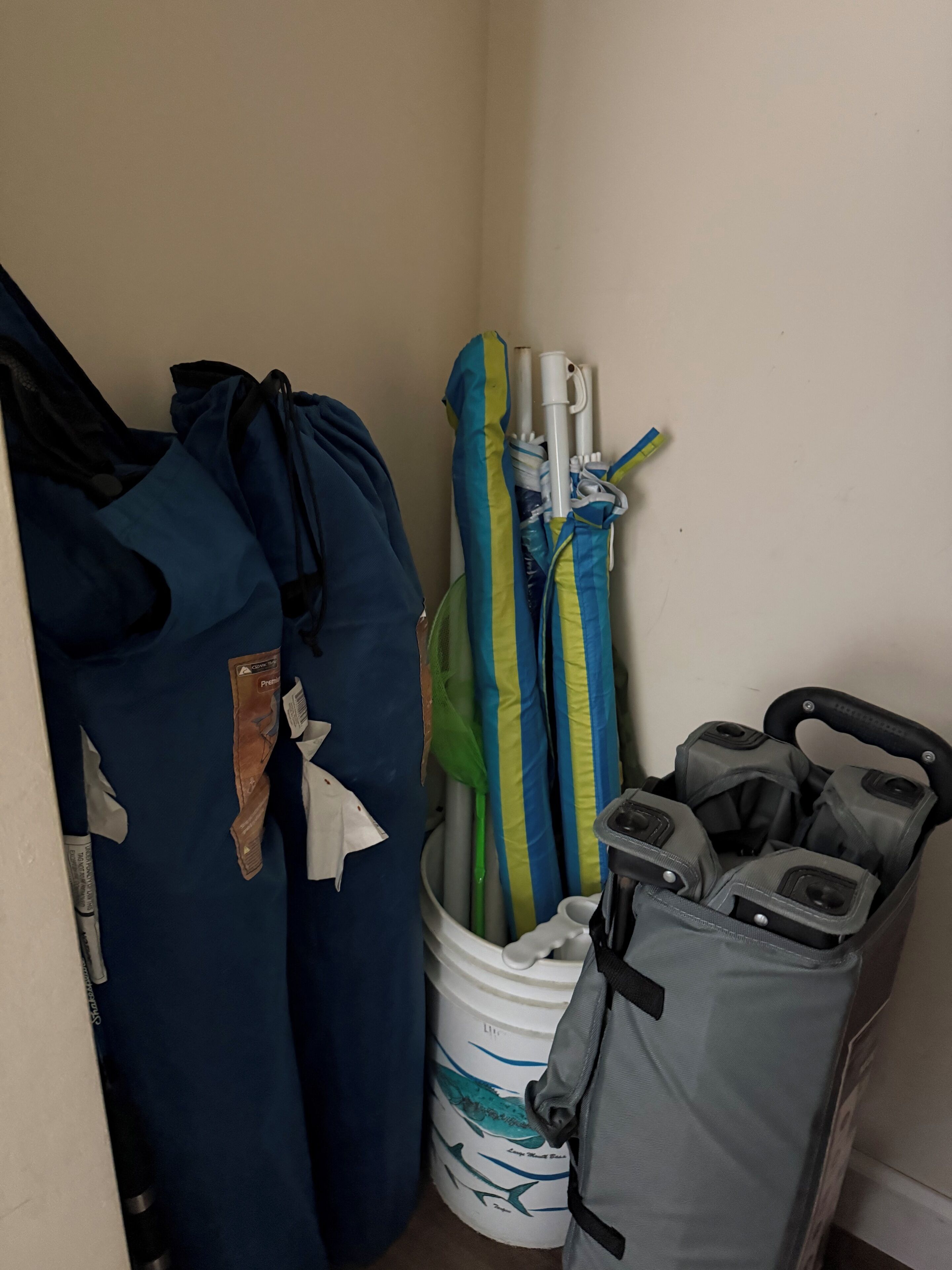 Un rincón de una habitación con un bolso azul, un cubo blanco con diseño de tiburón y un bolso gris.