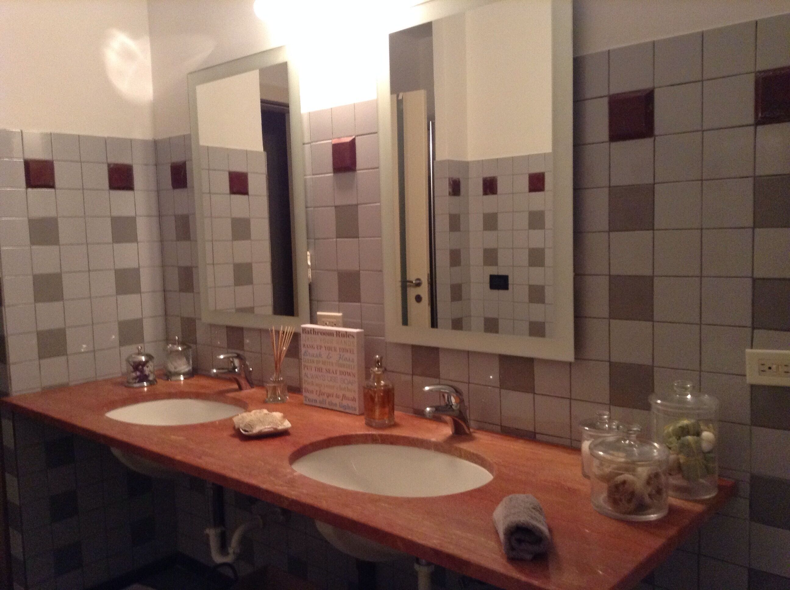 Un baño con dos lavamanos, un espejo y un cartel con las normas.