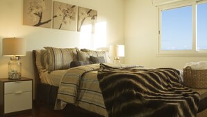 Un dormitorio con cama, mesitas de noche, lámparas y una obra de arte en la pared.