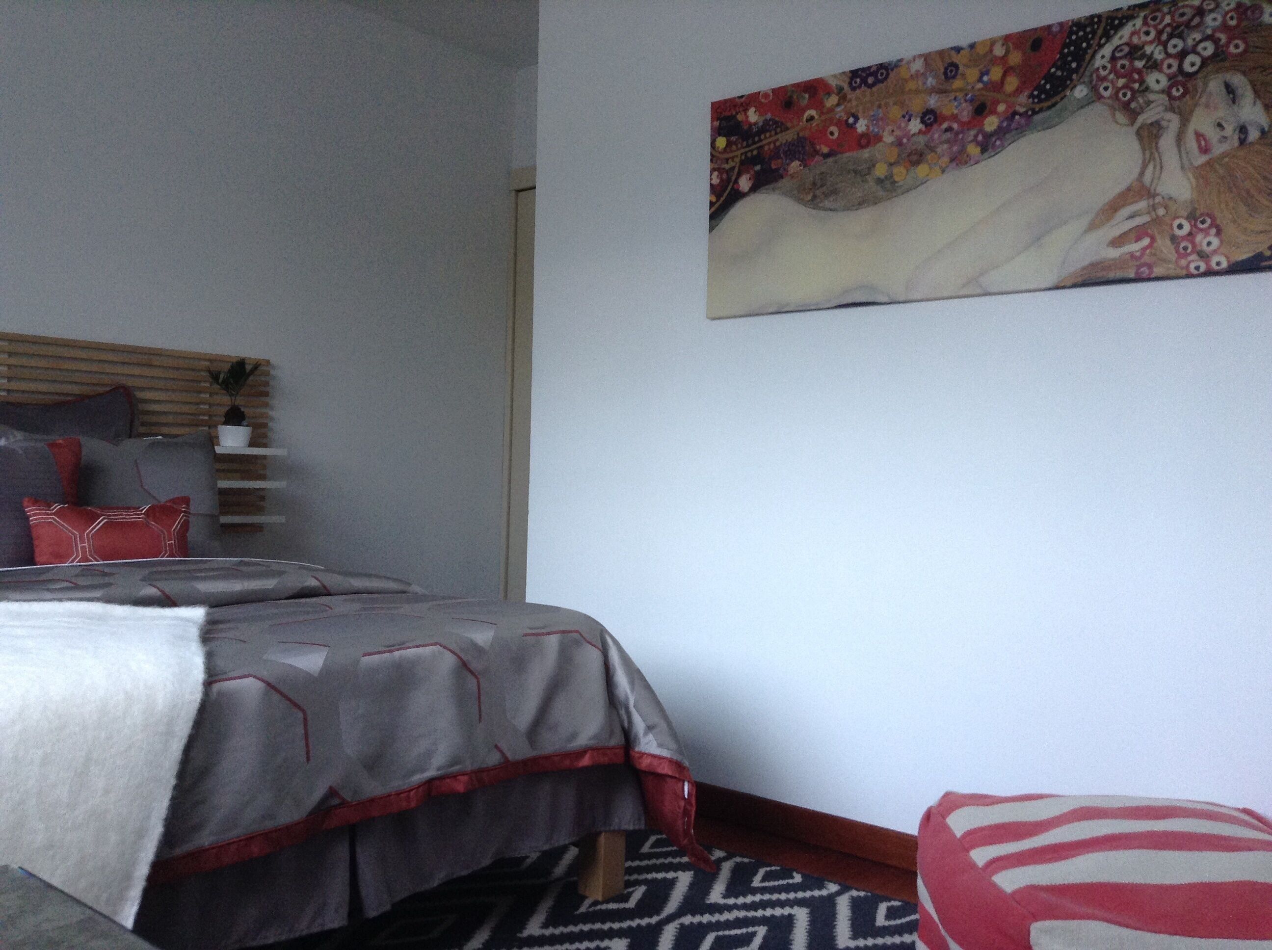 A bedroom with a bed, pillows, a bedside table, and a wall-mounted painting.