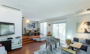 Un salon moderne avec un téléviseur à écran plat, une table basse et un canapé. Il y a également un coin repas avec une table et des chaises.