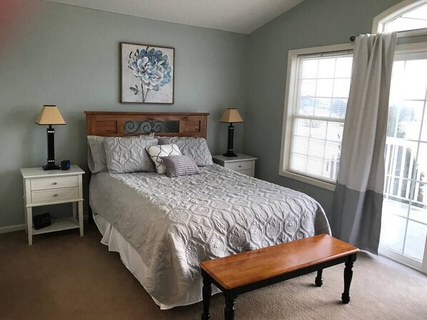 A bedroom with a bed, two bedside tables, a nightstand, a bench, a window with curtains, and a painting on the wall.
